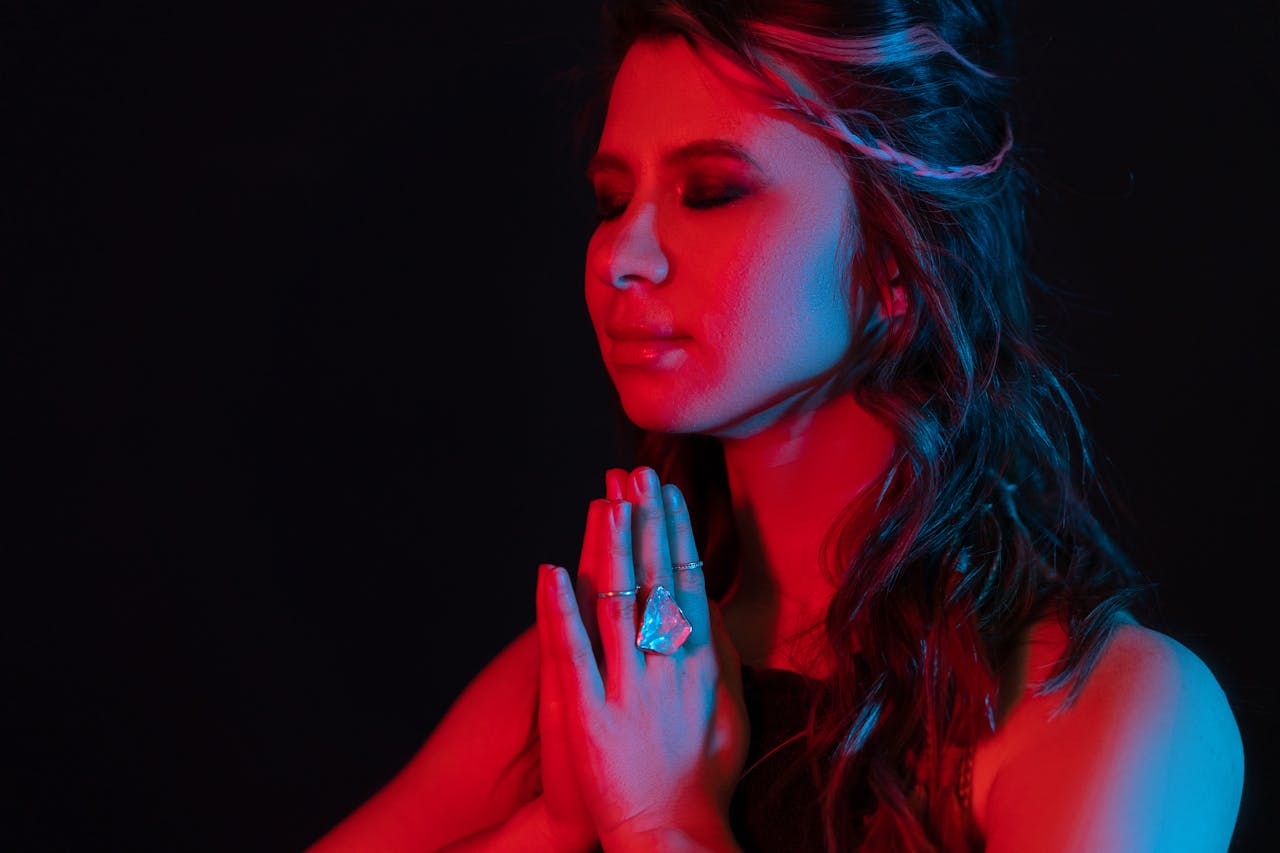 A woman meditates with hands in prayer, bathed in contrasting red and blue light.